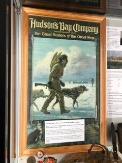 photograph of a framed poster in Stromness Museum. The poster is a recruitment poster depiicting a man  walking through the snow dressed in skins and carrying snow shoes on his back. He carries a shotgun in his right hand.  Two wolves/huskies accompany him.